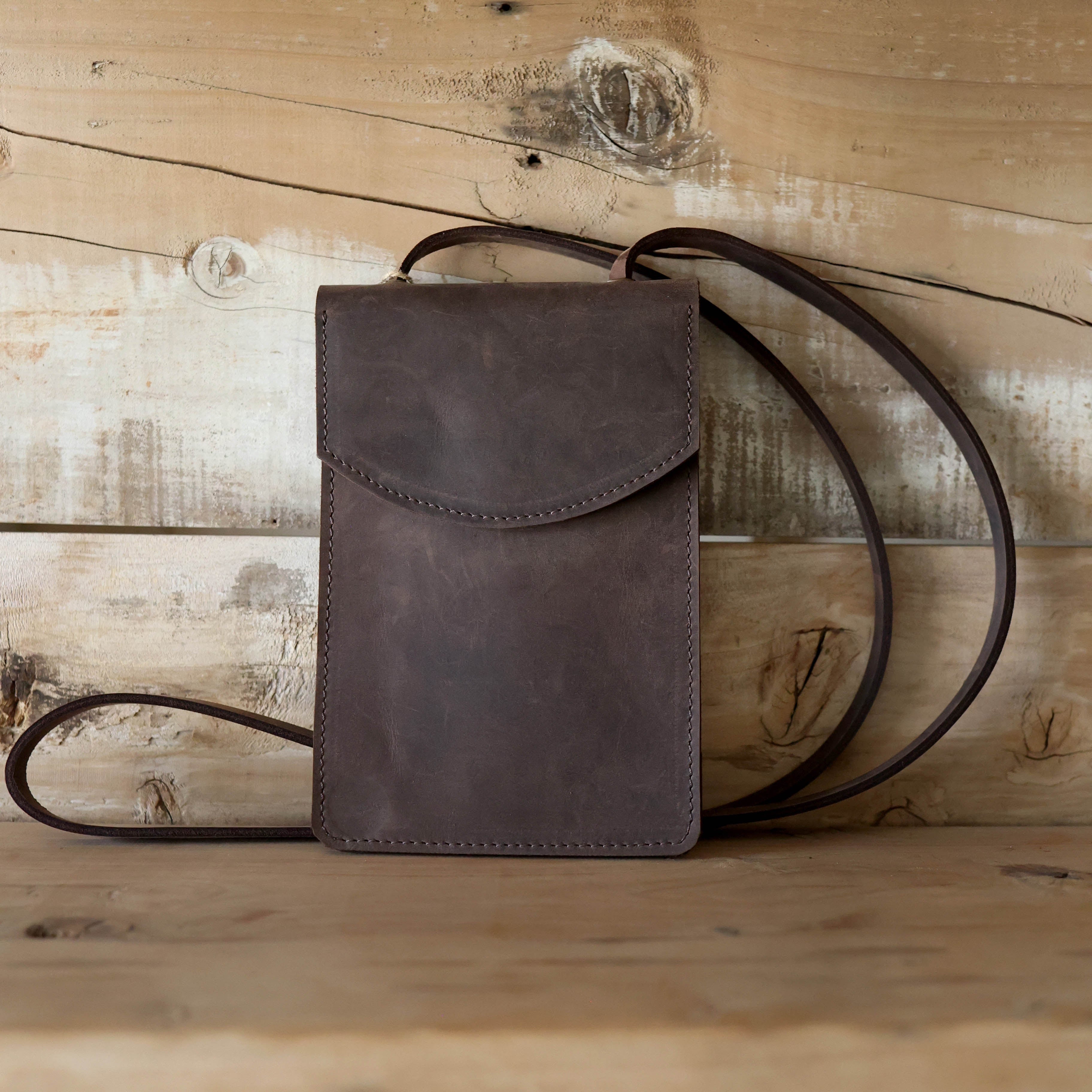 Brown leather bag with a strap on a wooden surface