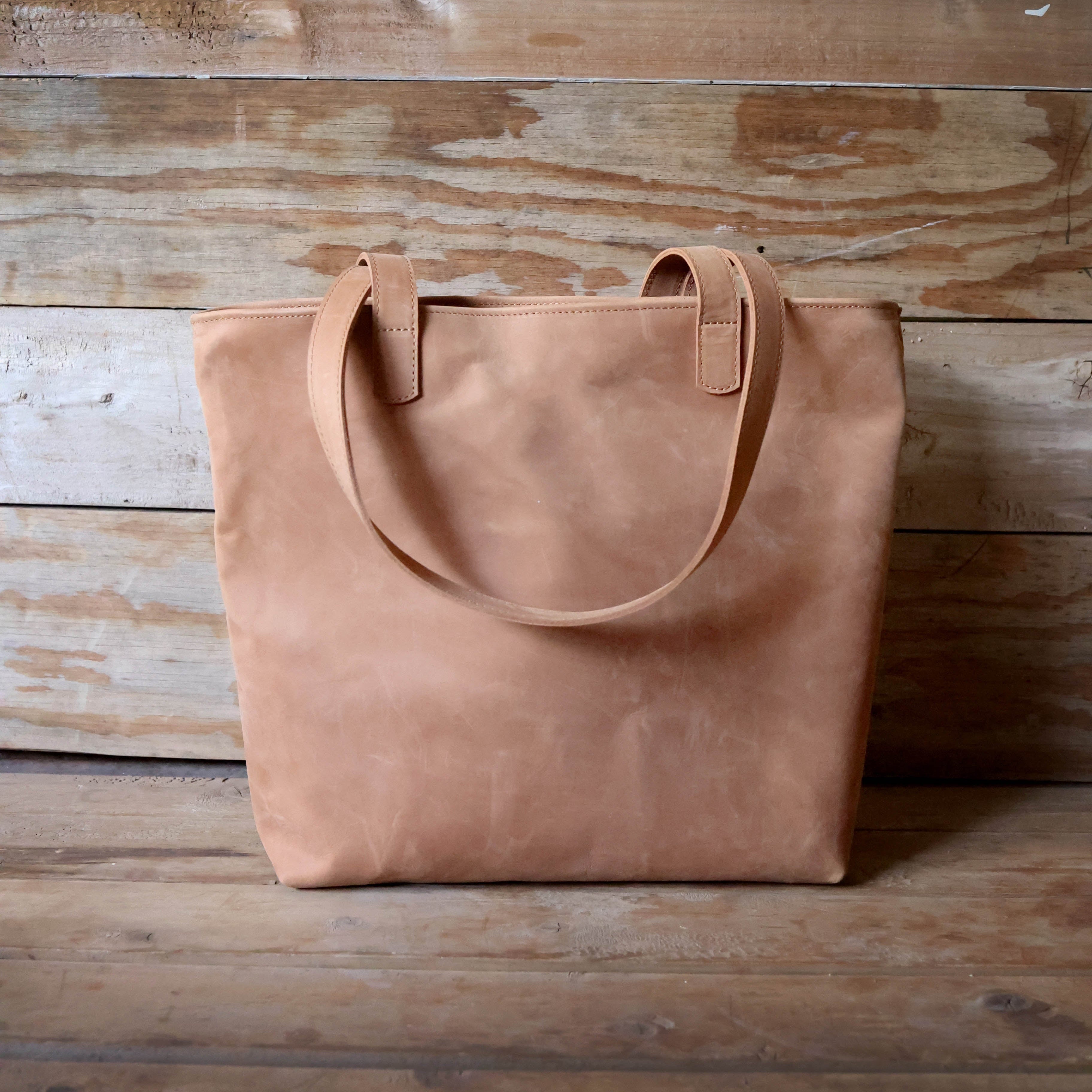 Brown leather tote bag on a wooden surface with a wooden background