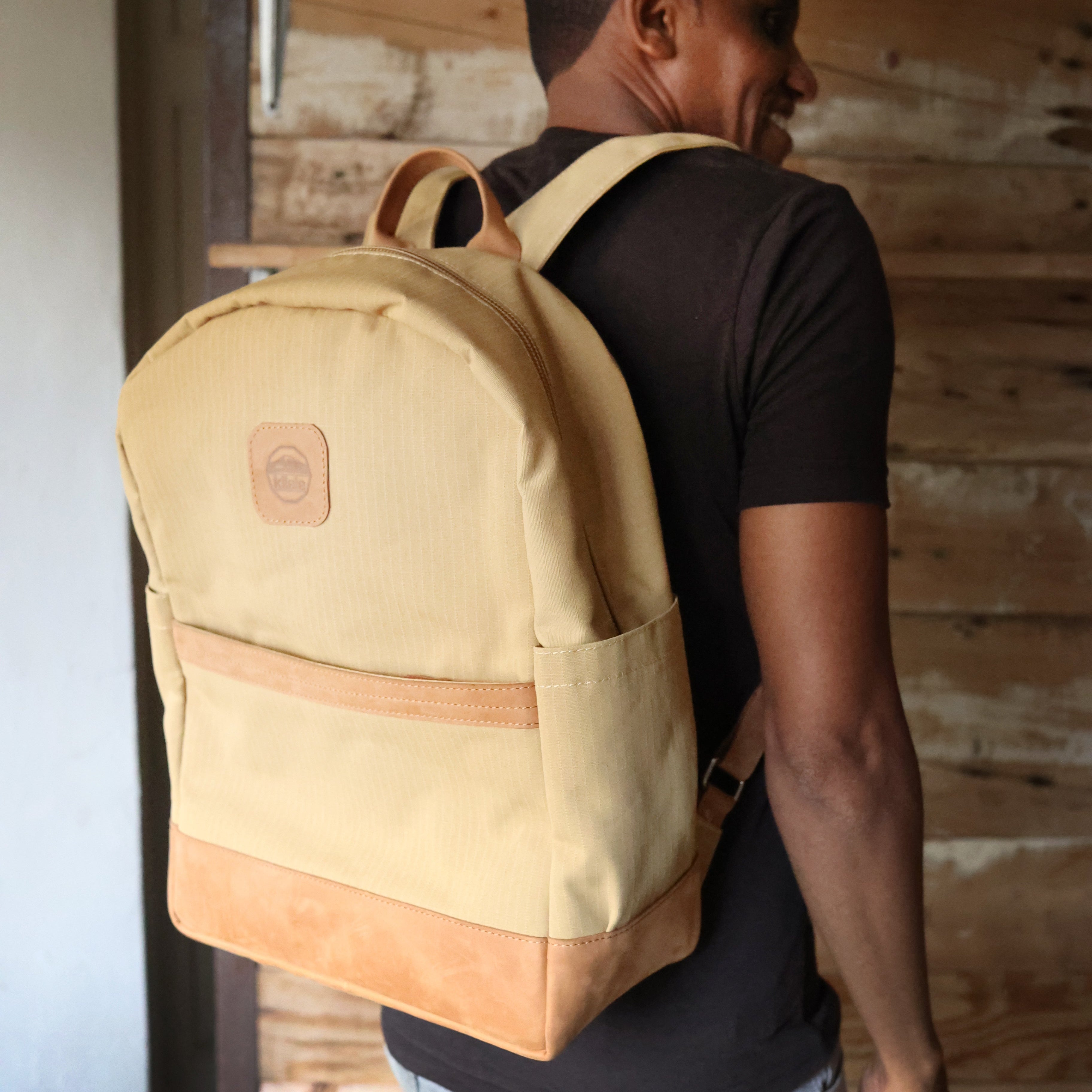 Man wearing a beige backpack indoors with wooden walls.
