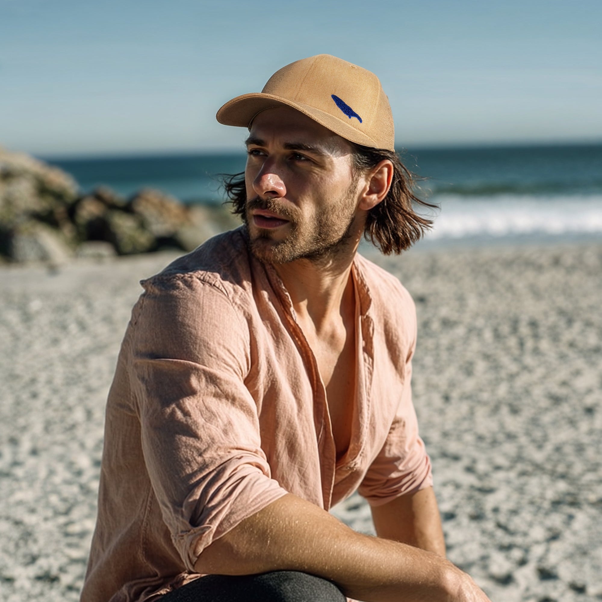 Man sitting on a beach wearing a beige cap and pink shirt