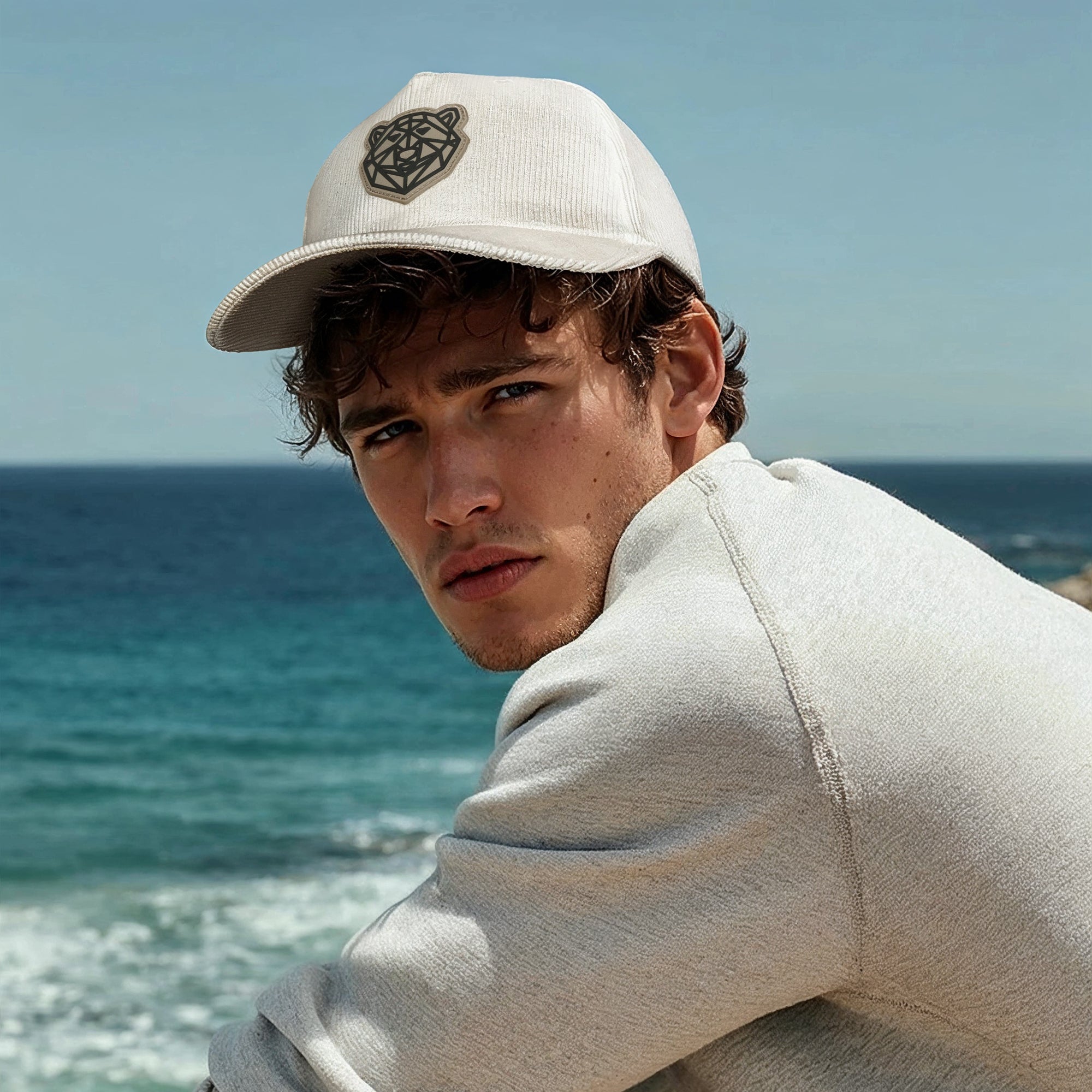 Man sitting on a rock by the ocean wearing the Arctic Protector II Corduroy Cap by Tembo Collection cap.