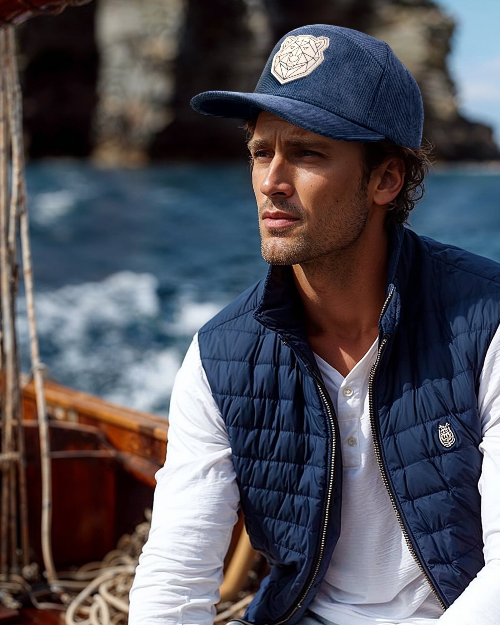 Man wearing a navy vest and cap on a boat with a scenic background