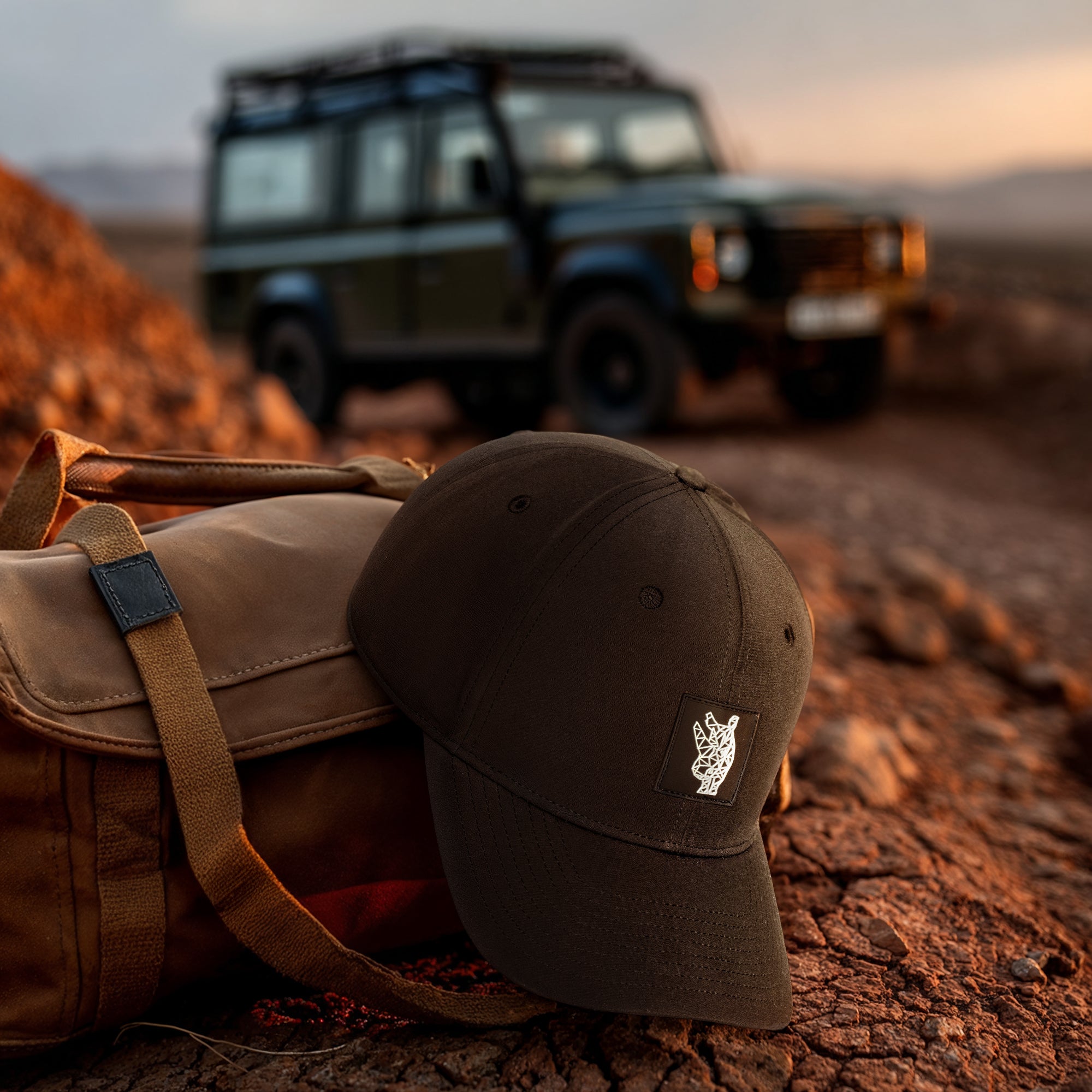 Brown cap and bag on a rocky terrain with a blurred off-road vehicle in the background