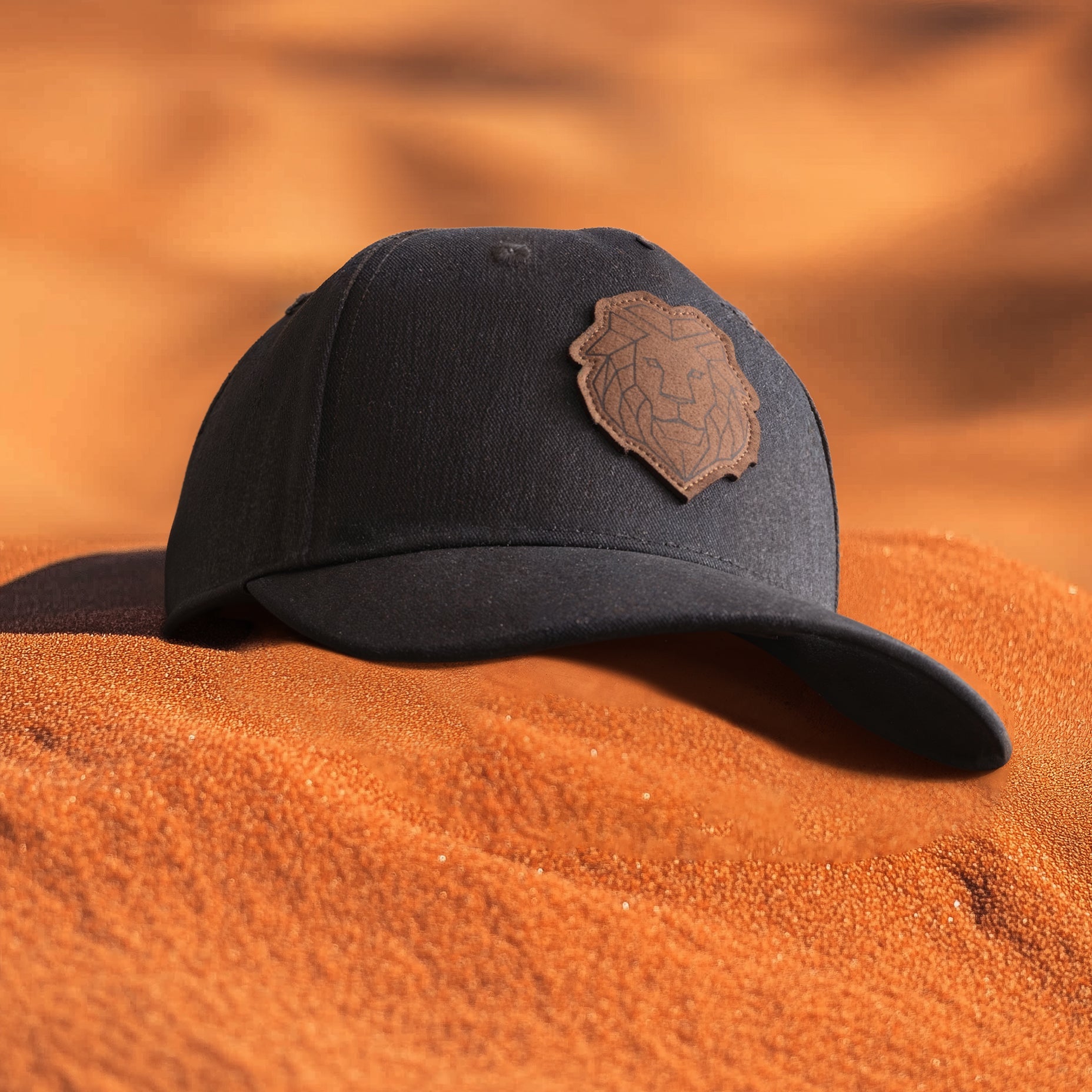 A green baseball cap with a leather patch featuring a geometric lion face on the front, placed on a rocky surface.