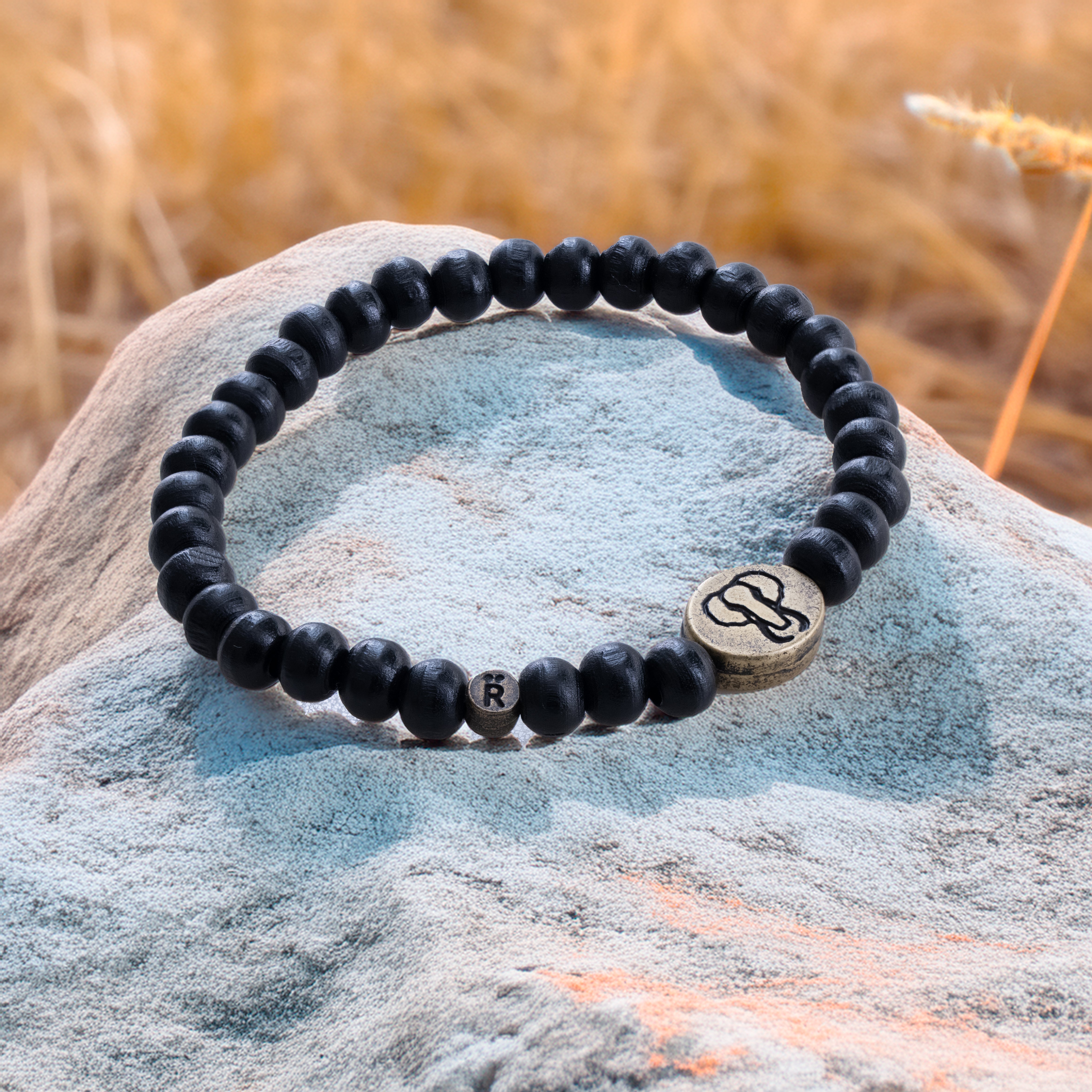 A black beaded bracelet with a metallic charm, displayed on a rock.