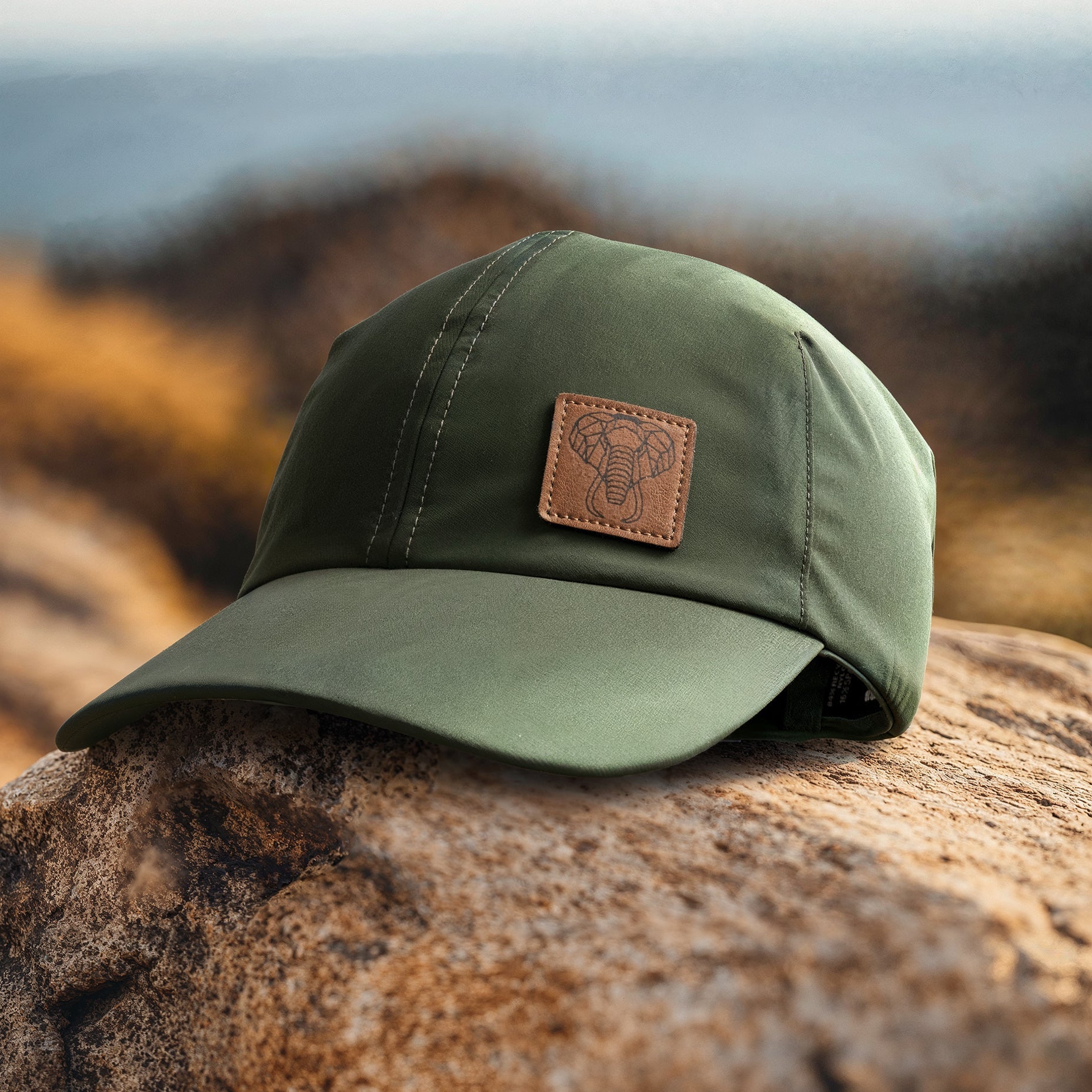 A green baseball cap with a leather patch on the front, placed on a rock with a blurred natural background.