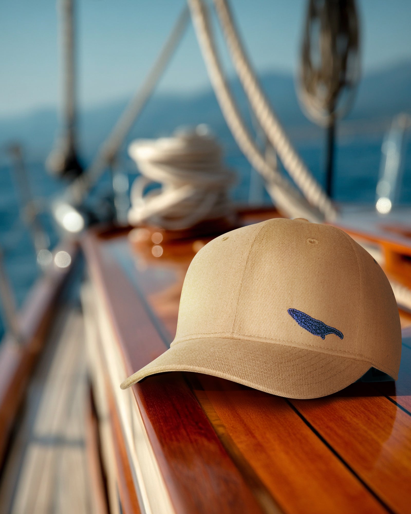 Beige cap with a logo on a sailboat deck with ocean and mountains in the background