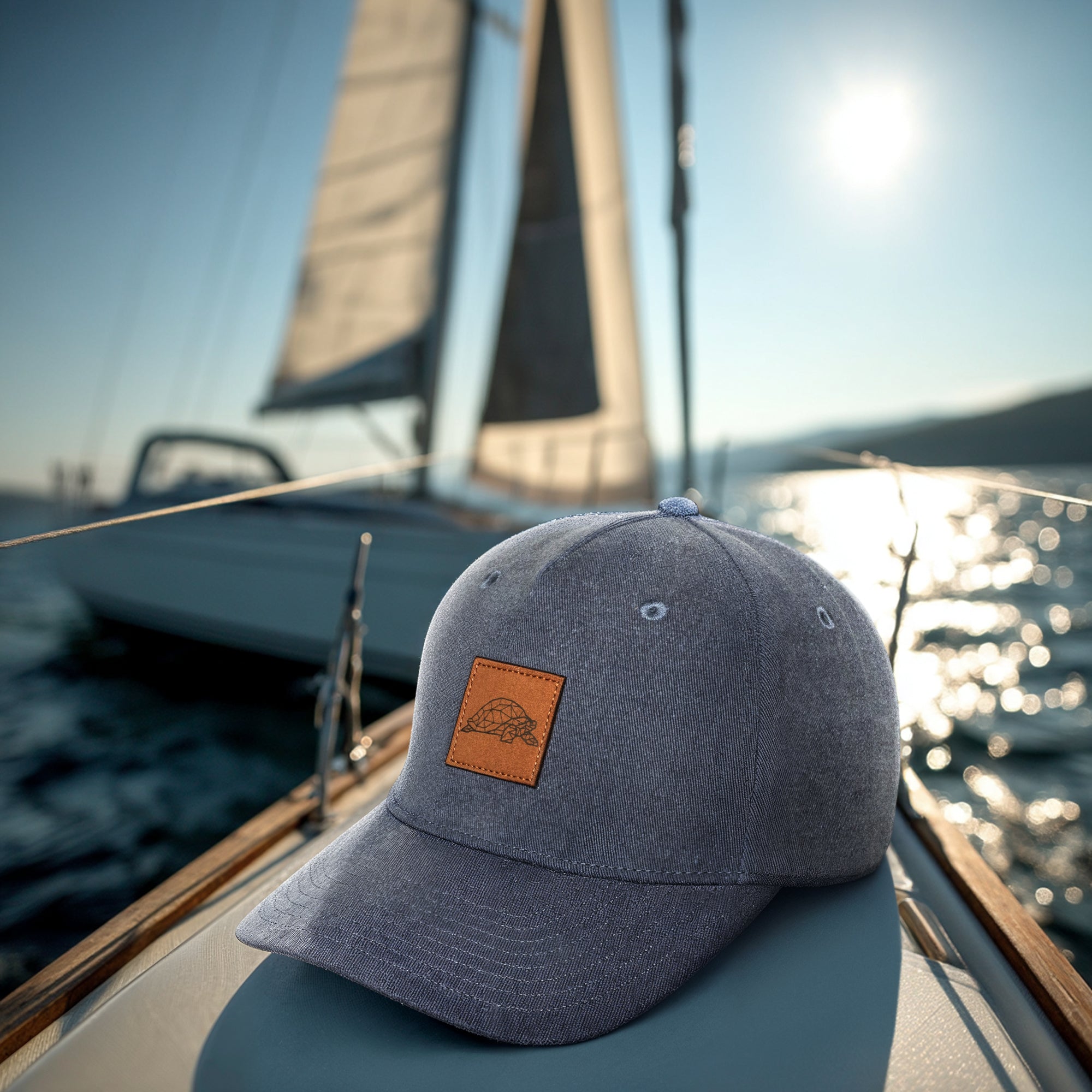 Blue cap with a leather patch on a boat with a sail in the background