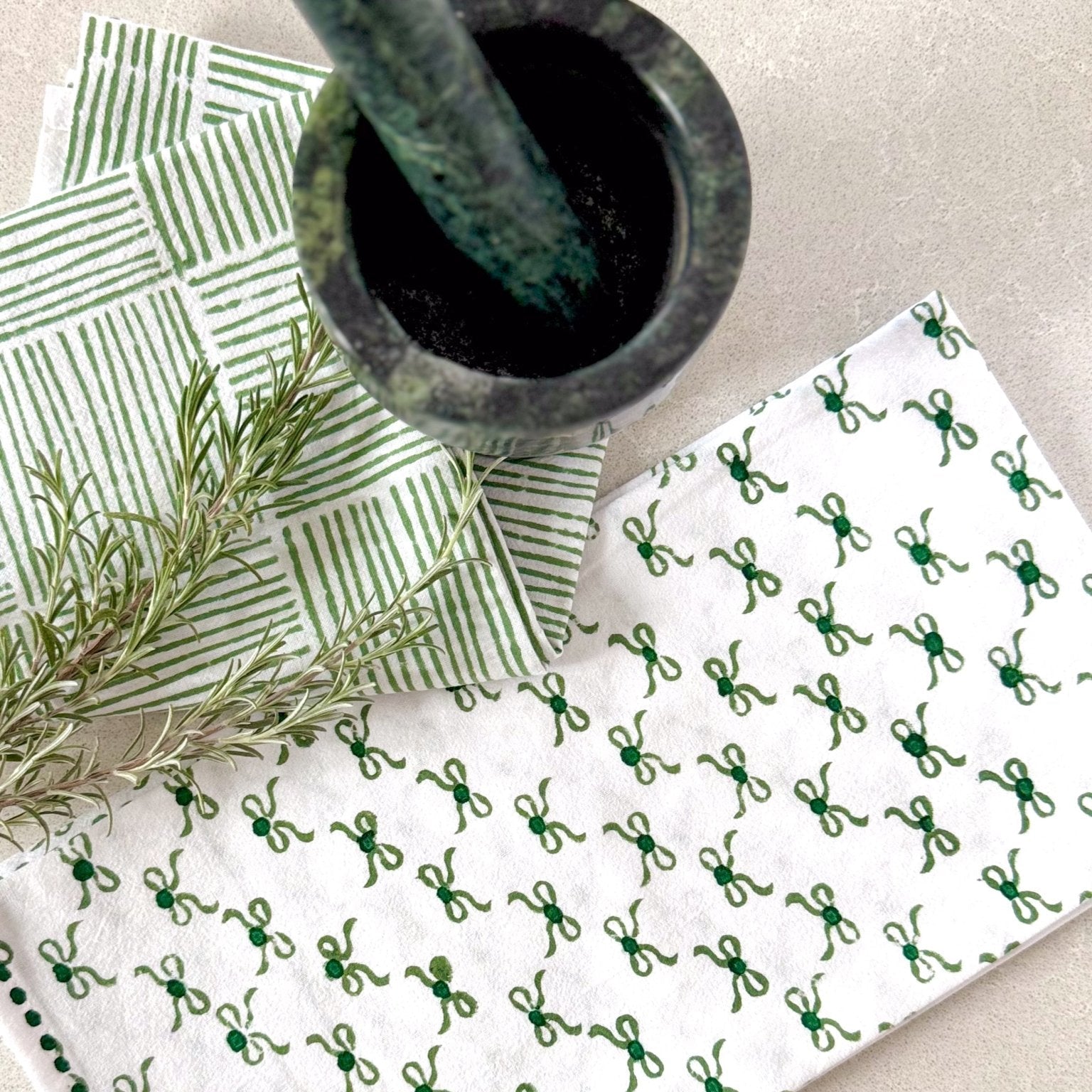 White cloth with green pattern, green leaves, and a mortar and pestle on a light background