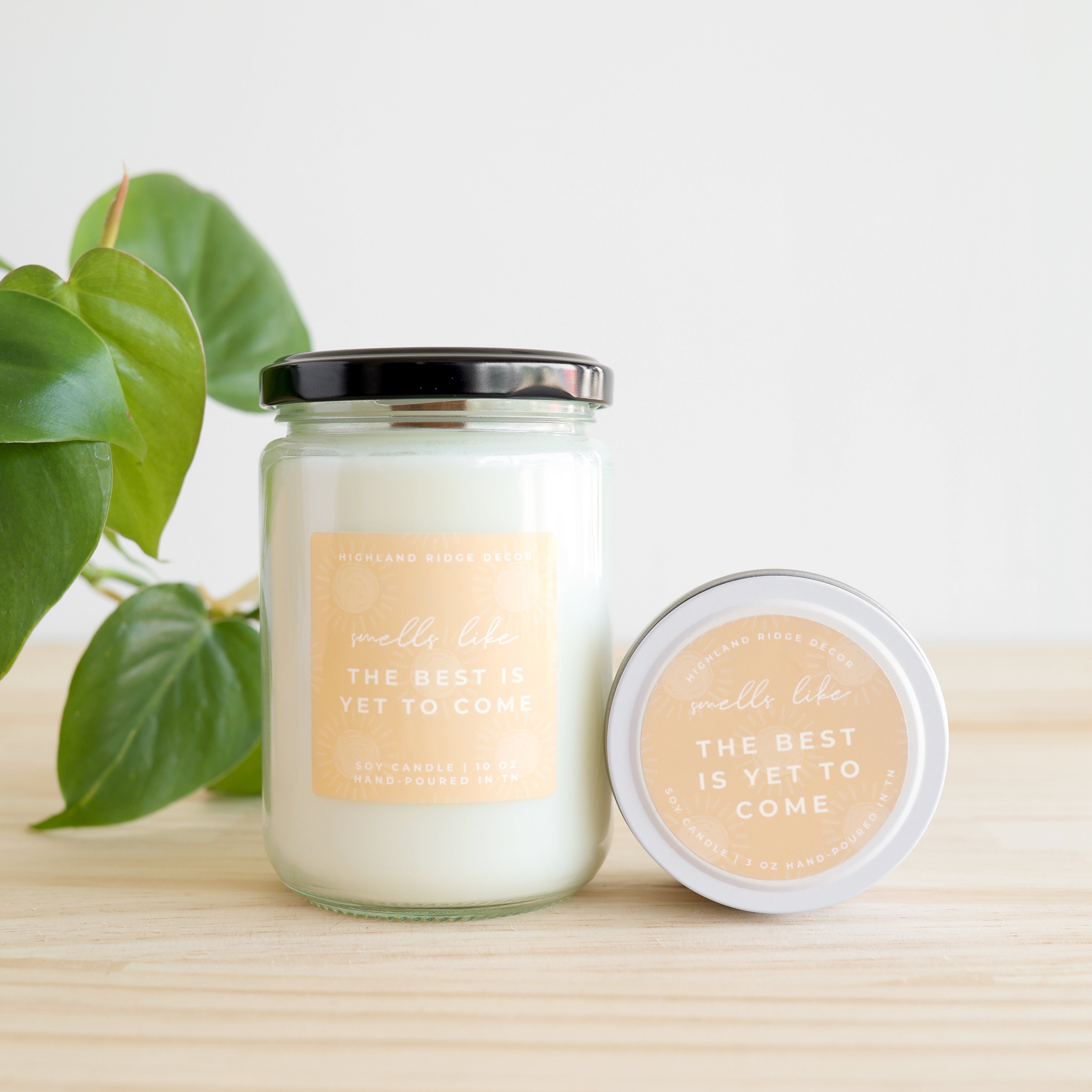 Candle with a label on a wooden surface with a plant in the background