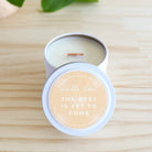 Cosmetic compact with 'The best is yet to come' text on a wooden surface with a plant in the corner.