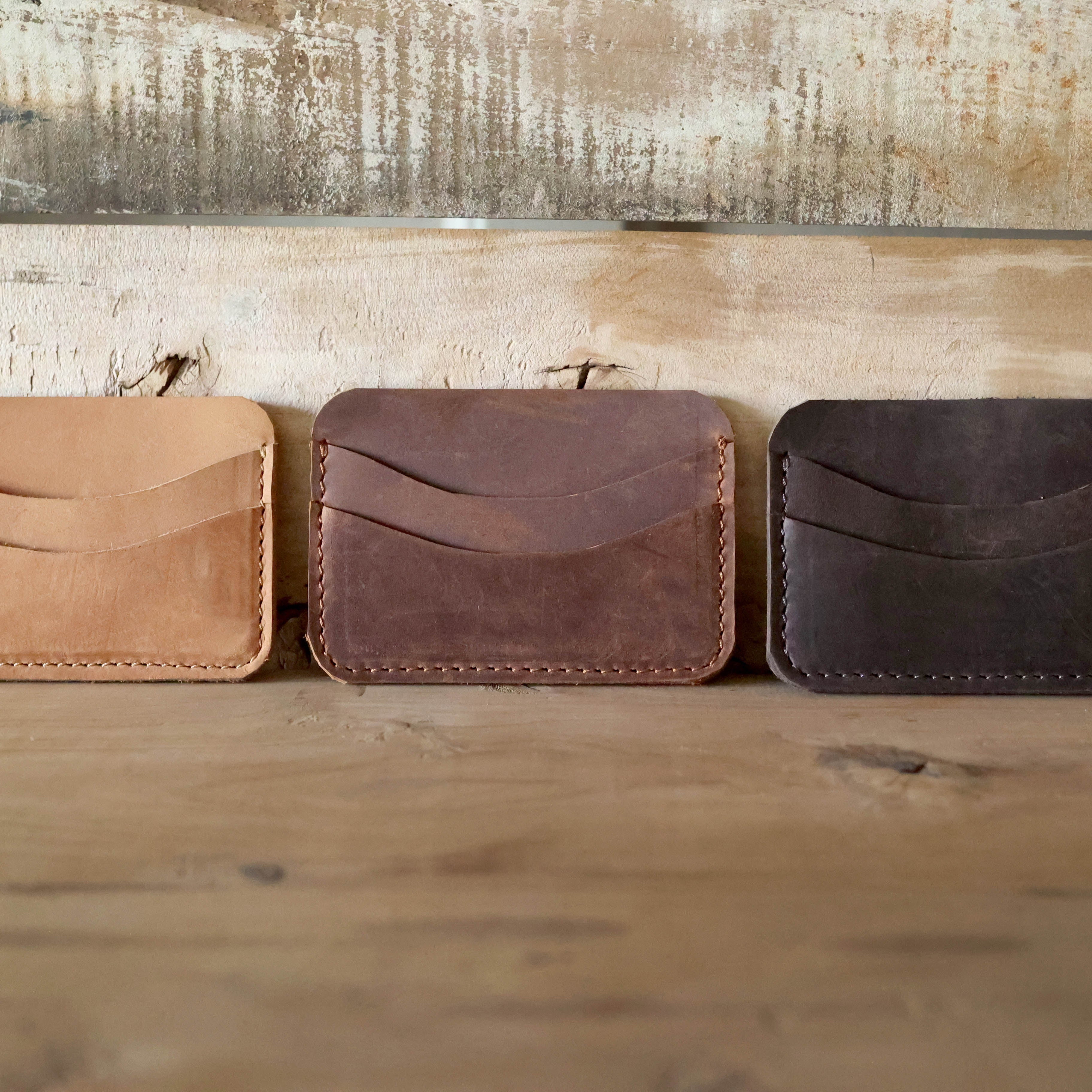 Three leather card holders in different colors on a wooden surface with a rustic background.