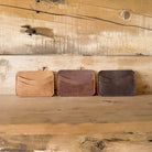 Three leather wallets in different colors on a wooden surface