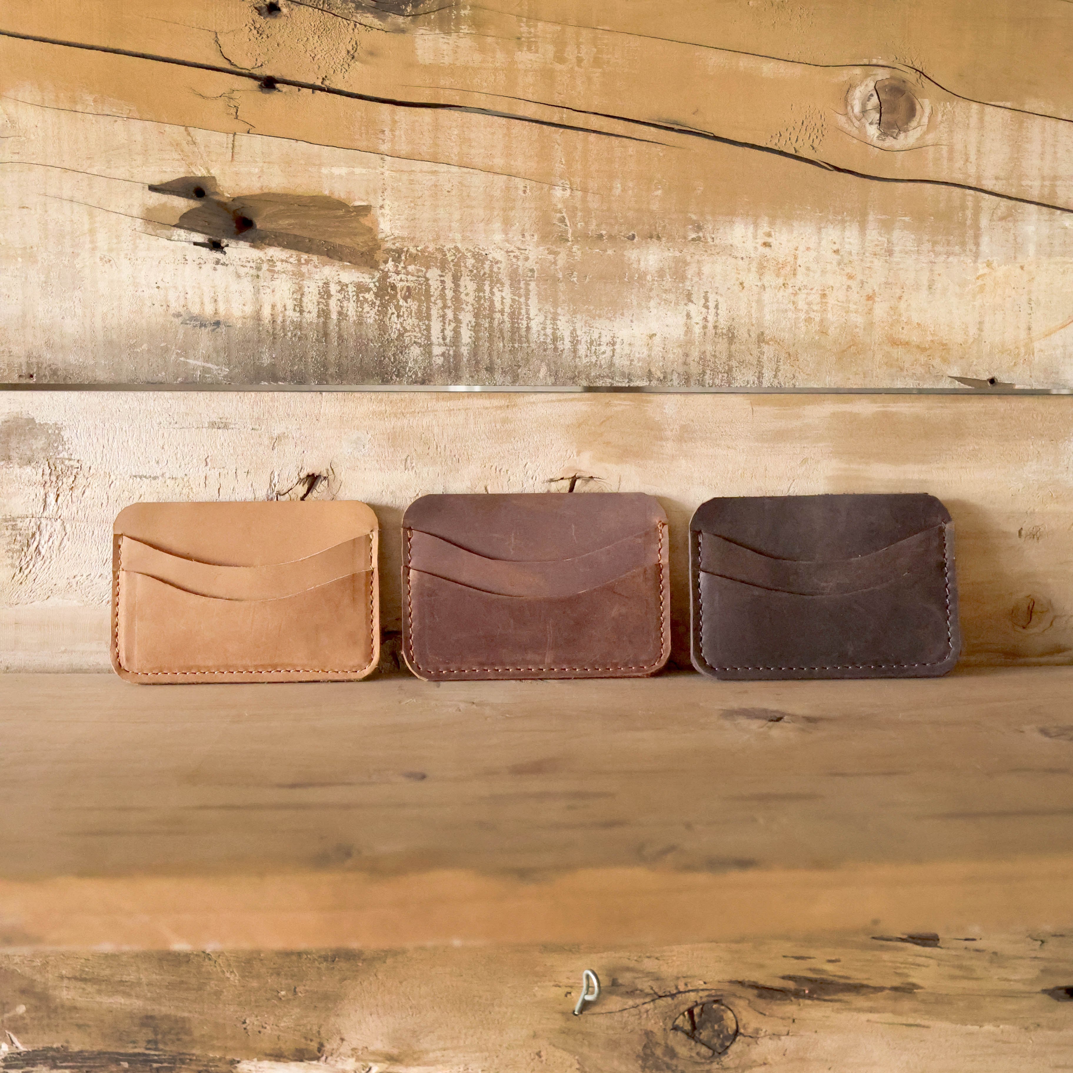 Three leather wallets in different colors on a wooden surface