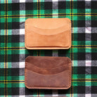 Three leather card holders on a green plaid fabric background
