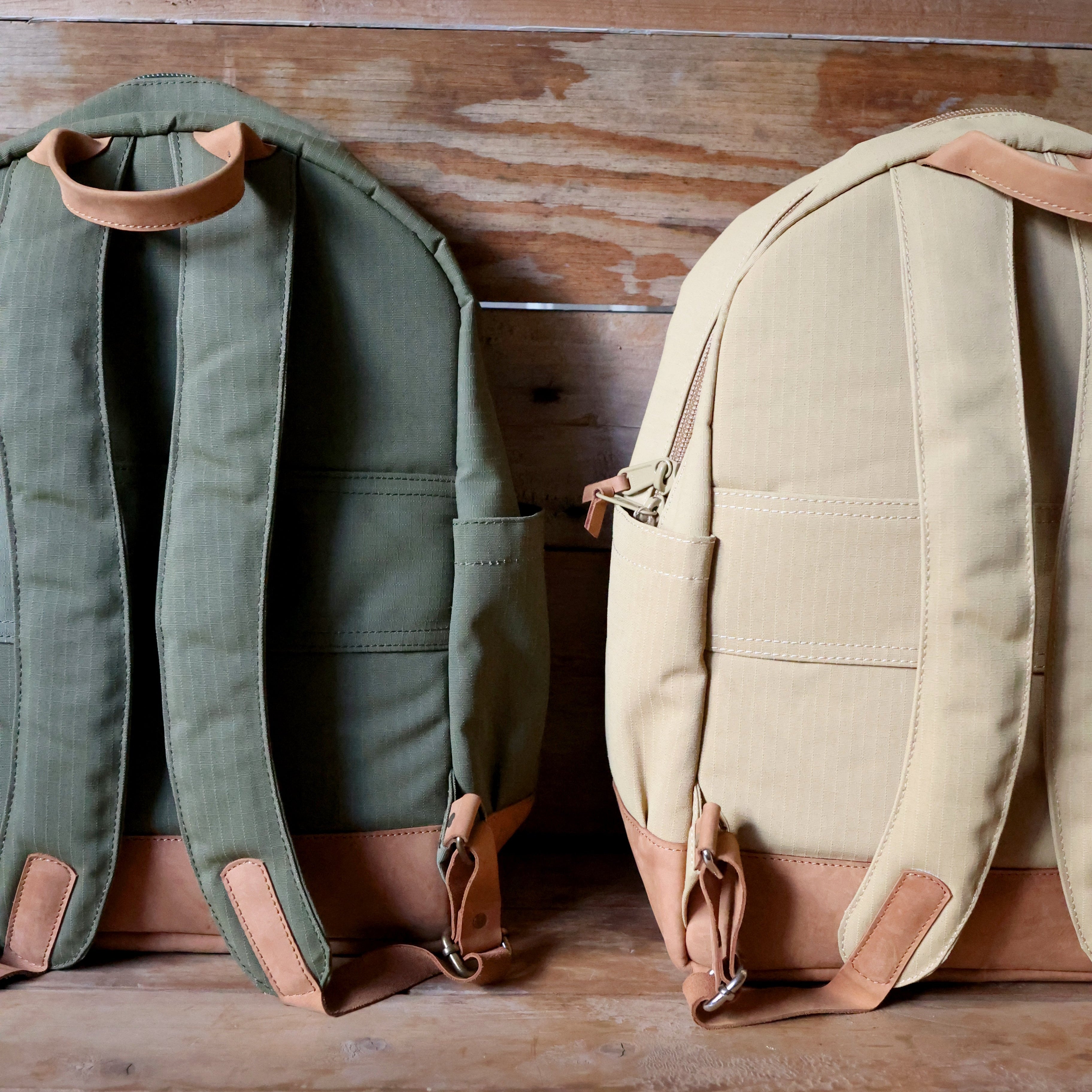 Two backpacks, one green and one beige, on a wooden surface.