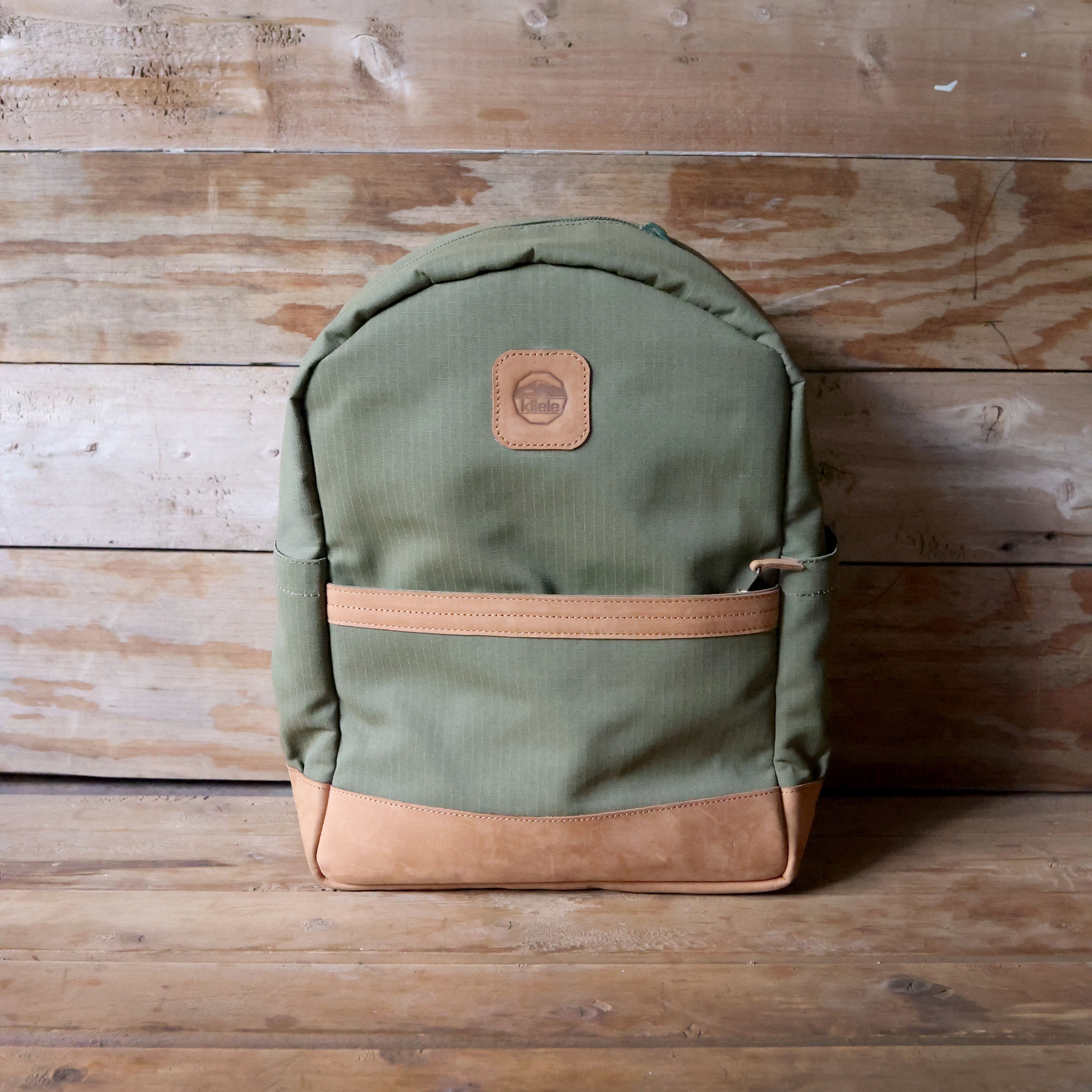 Green backpack with brown accents on a wooden surface