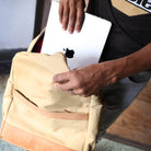 Person holding a beige backpack with a laptop, wearing a black t-shirt with 'kilele' branding.