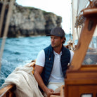 Man on a sailboat with rocky cliffs in the background