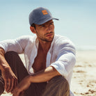 Man sitting on a beach wearing a cap and white shirt
