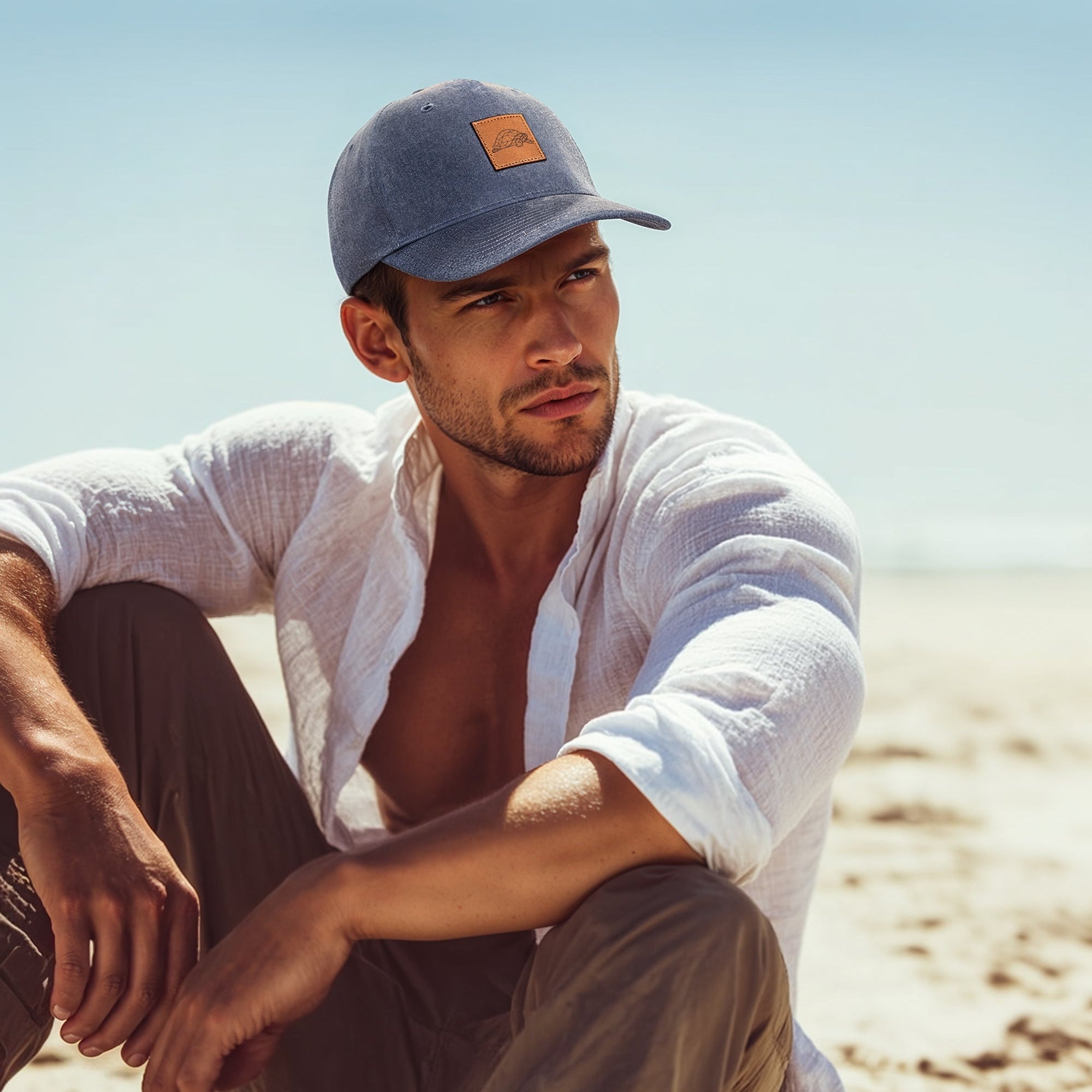 Man sitting on a beach wearing a cap and white shirt