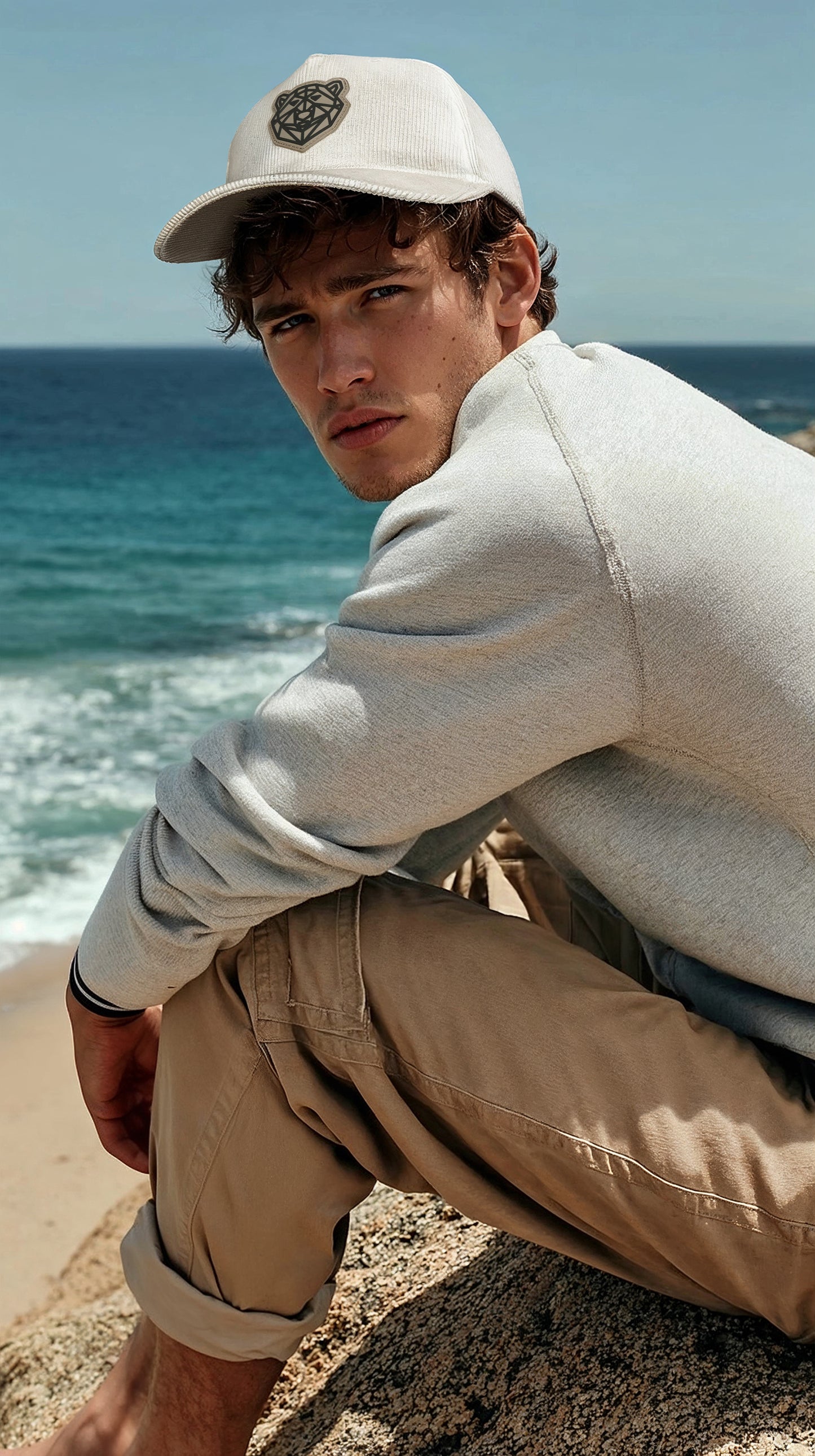 Man sitting on a rock by the ocean wearing the Arctic Protector II Corduroy Cap by Tembo Collection cap.