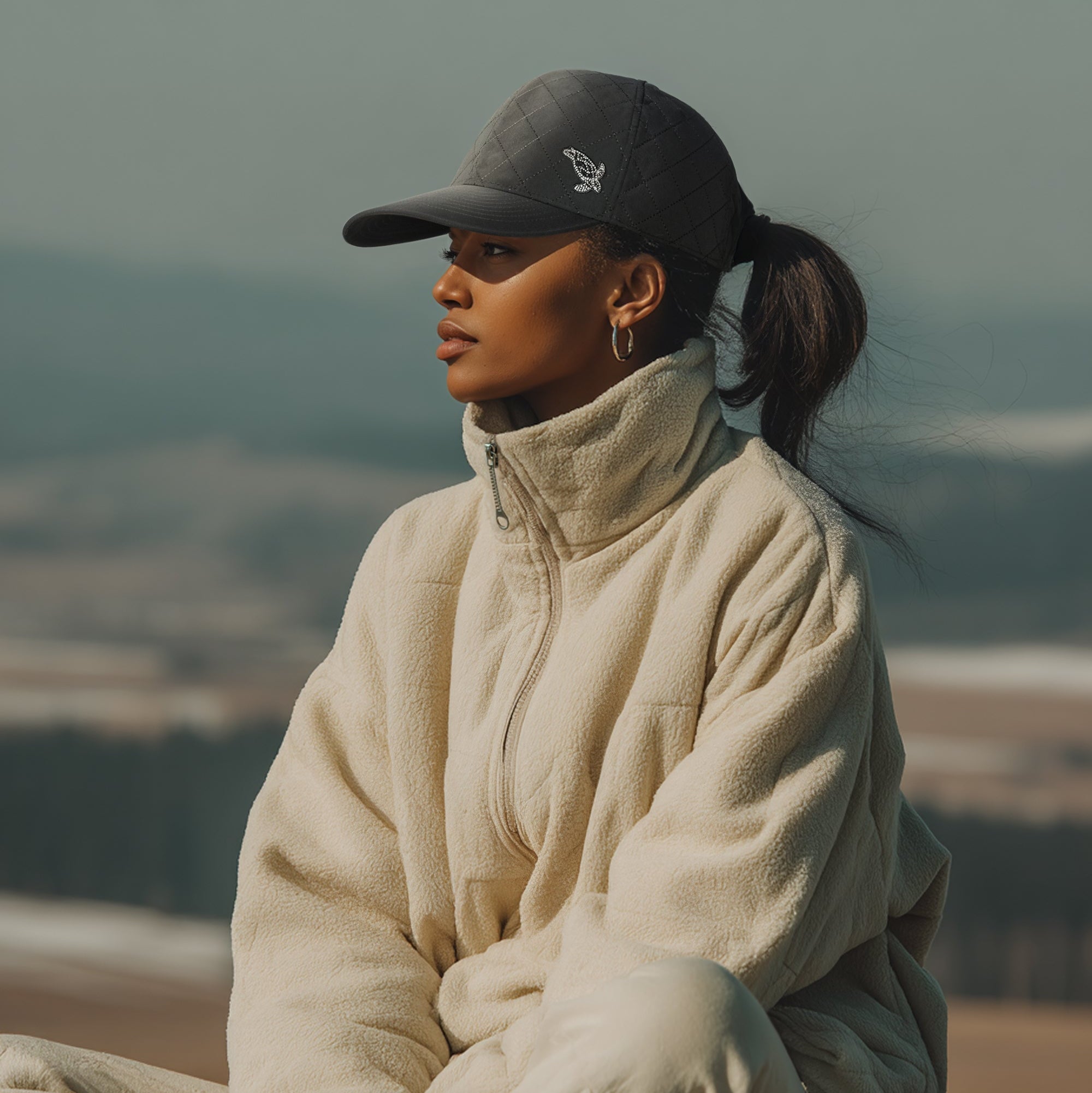Person wearing a cap and beige jacket sitting outdoors with a blurred natural background