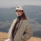 Woman wearing the Arctic Protector II Corduroy Cap by Tembo Collection and jacket standing in a field with mountains in the background