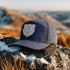 Navy blue cap with bear emblem on a rocky surface with a mountainous background