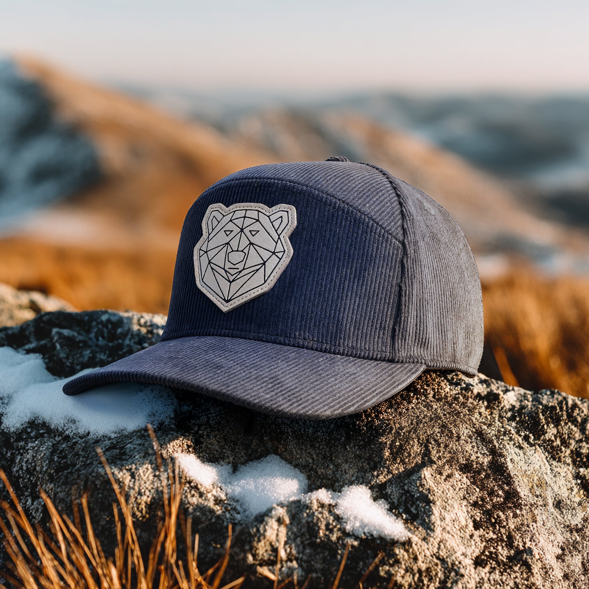 Navy blue cap with bear emblem on a rocky surface with a mountainous background