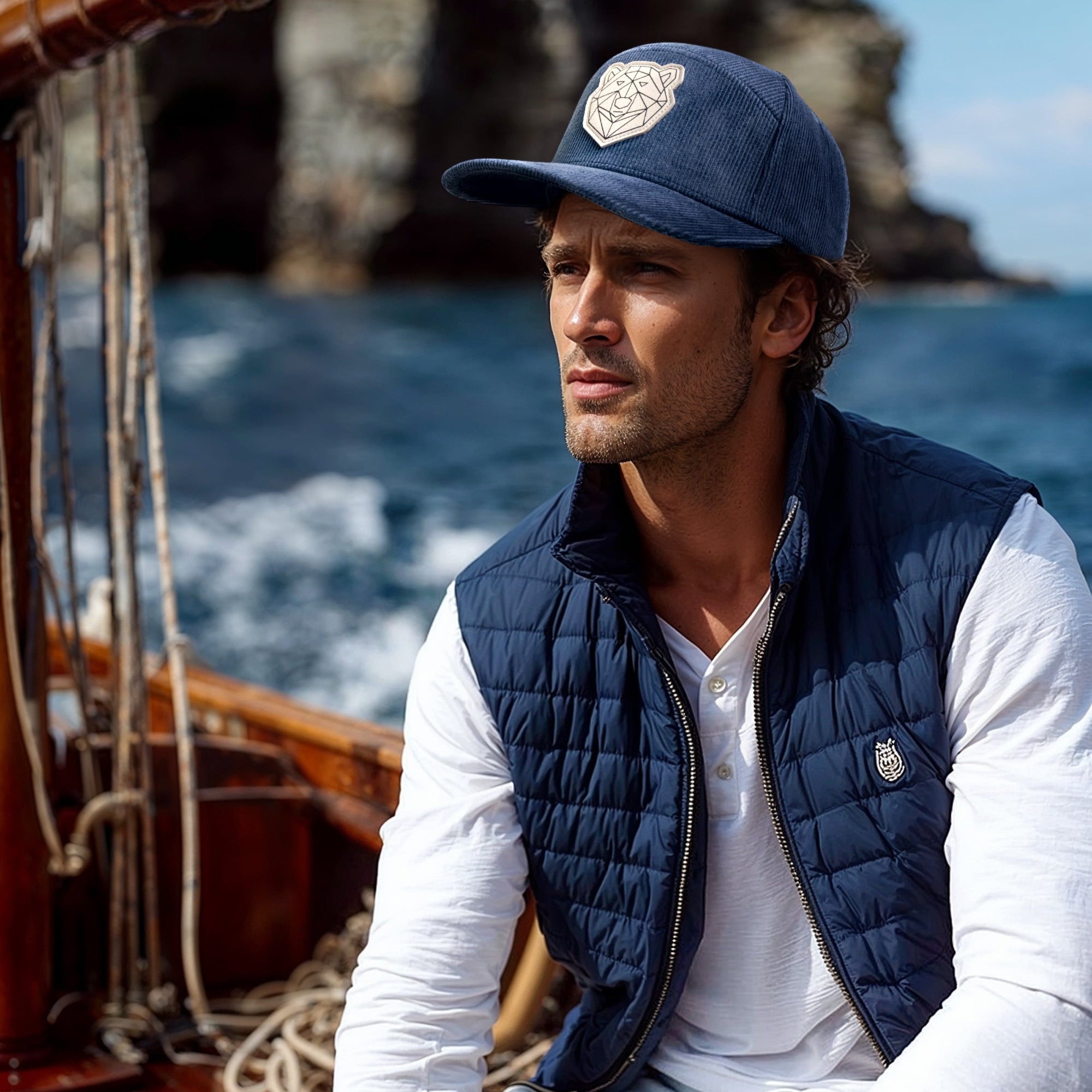 Man wearing a navy vest and cap on a boat with a scenic background