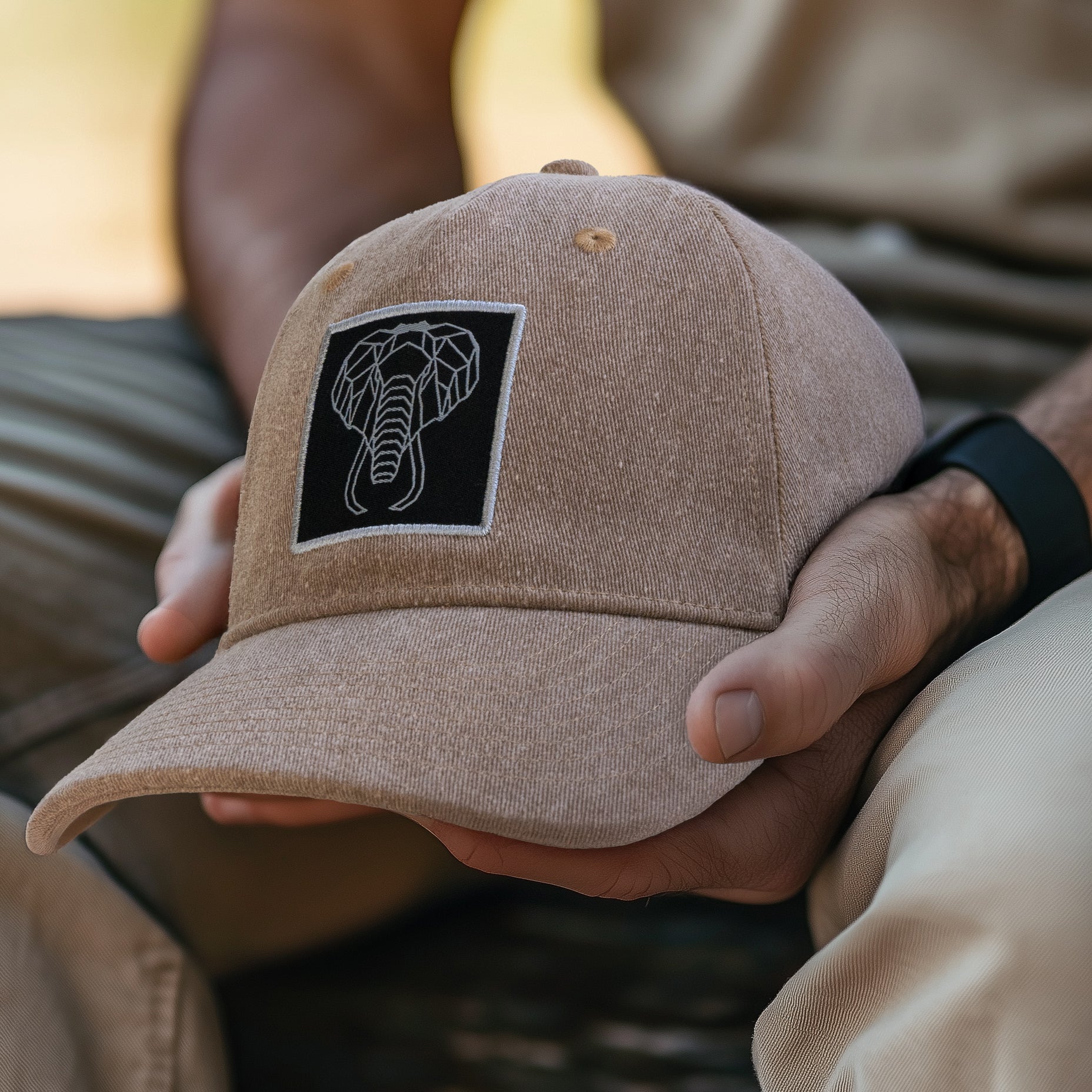 Beige cap with a logo held by a person in a natural setting