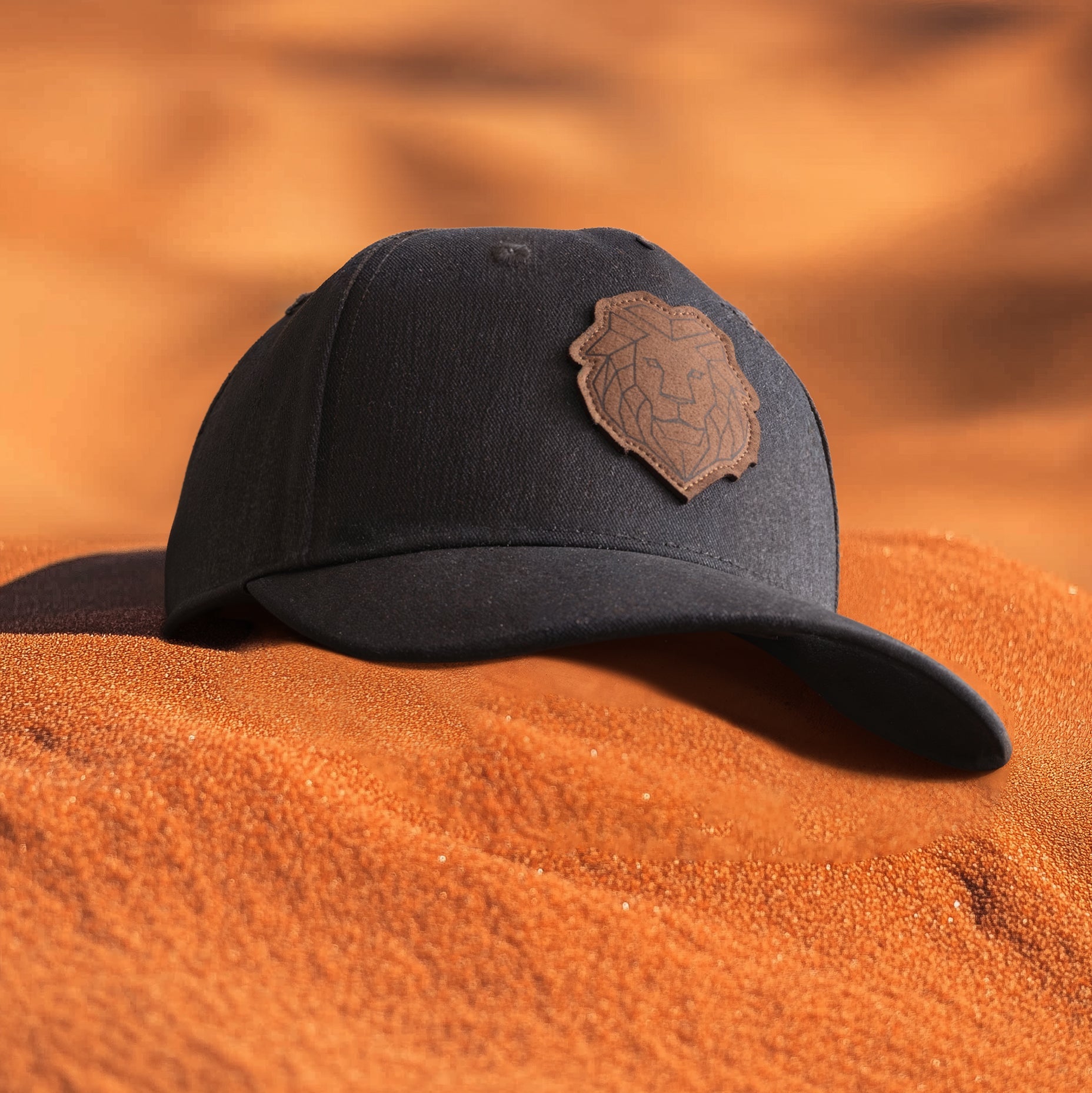 A green baseball cap with a leather patch featuring a geometric lion face on the front, placed on a rocky surface.