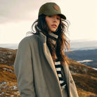 Woman wearing a green cap and coat standing on a mountain with a scenic background