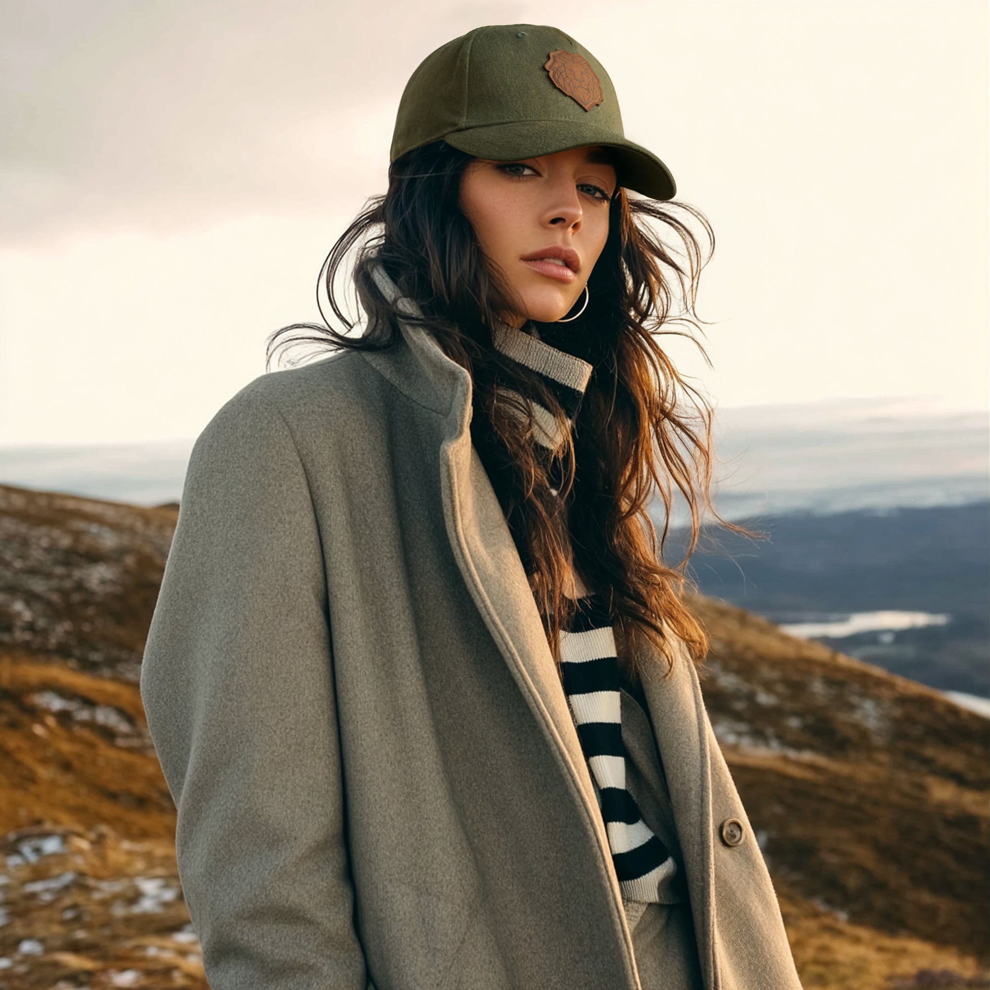 Woman wearing a green cap and coat standing on a mountain with a scenic background