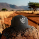 Black cap with a geometric animal logo on a rock in a desert landscape