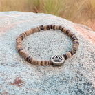 A beaded bracelet with a geometric patterned charm, displayed on a rock.