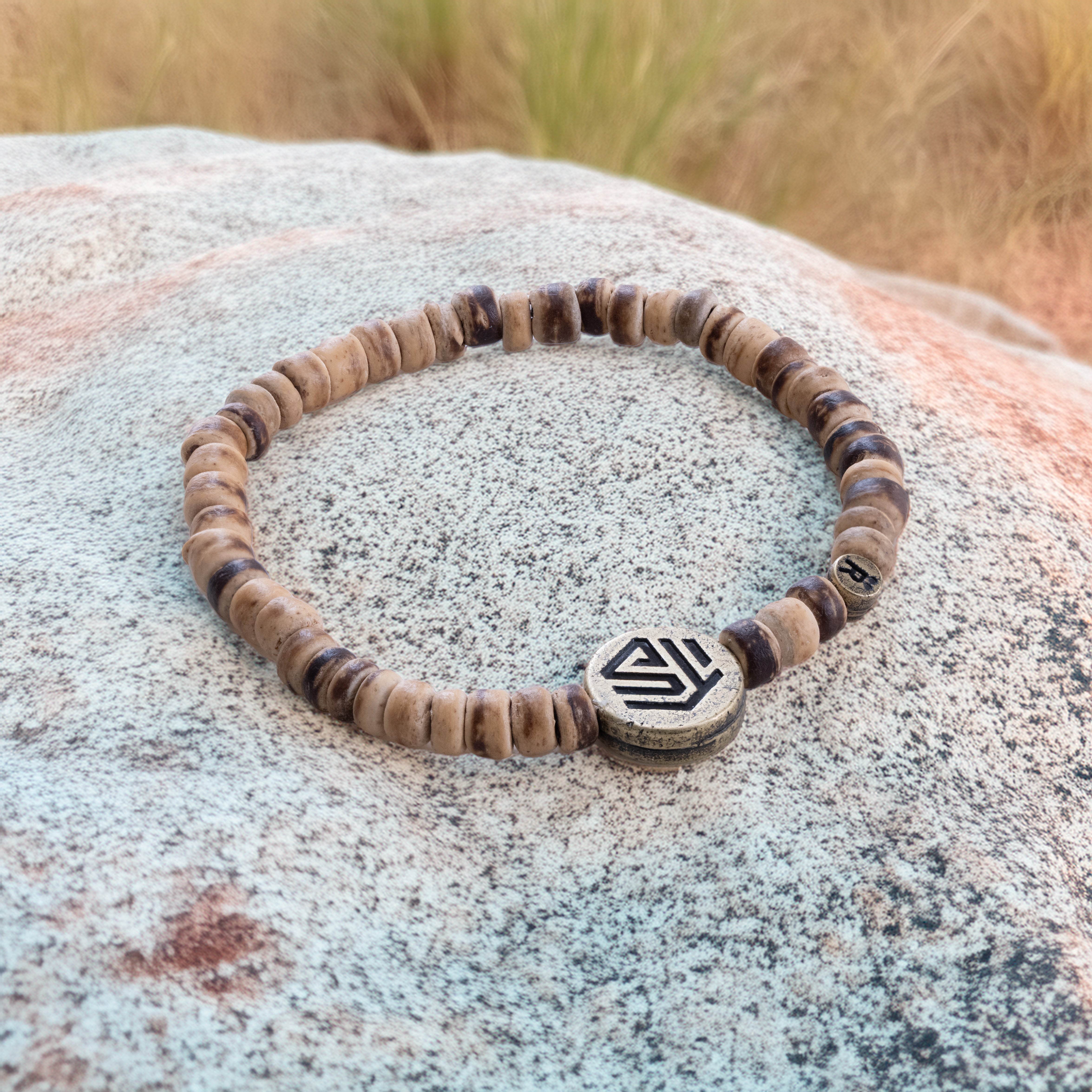 A beaded bracelet with a geometric patterned charm, displayed on a rock.