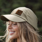 A green baseball cap with a leather patch on the front, placed on a rock with a blurred natural background.