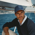 Man wearing a navy sweater and blue cap on a sailboat