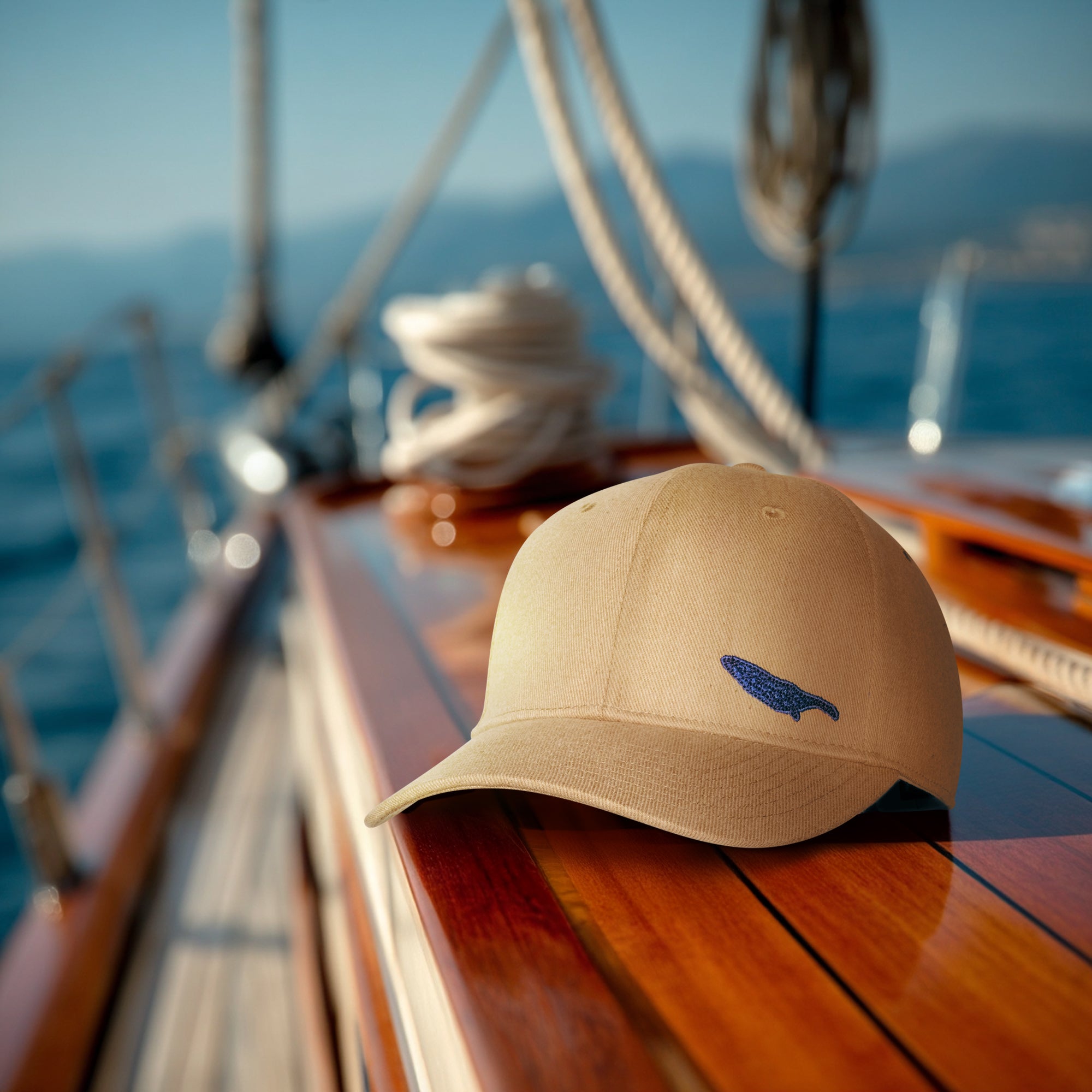 Beige cap with a logo on a sailboat deck with ocean and mountains in the background