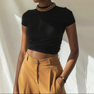 Woman wearing a black top and mustard pants against a neutral background