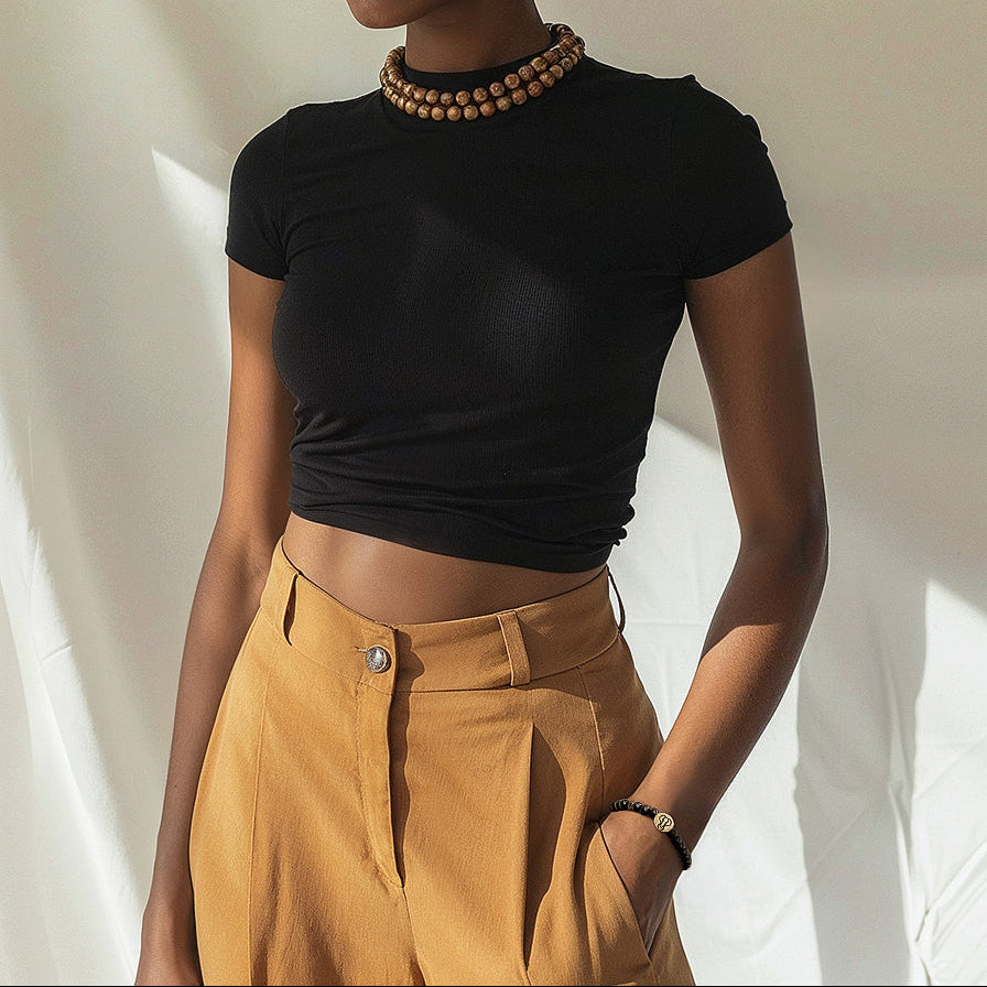 Woman wearing a black top and mustard pants against a neutral background