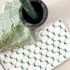 White cloth with green pattern, green leaves, and a mortar and pestle on a light background