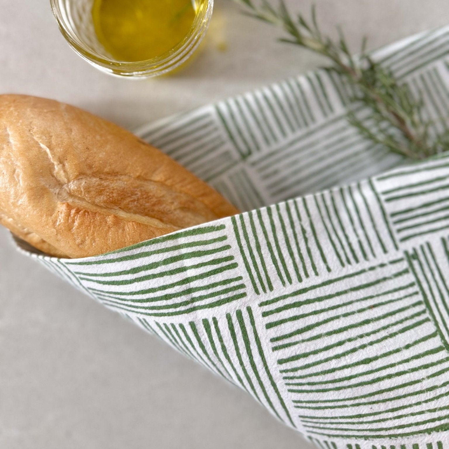 Bread in a patterned basket with olive oil and rosemary on a light surface
